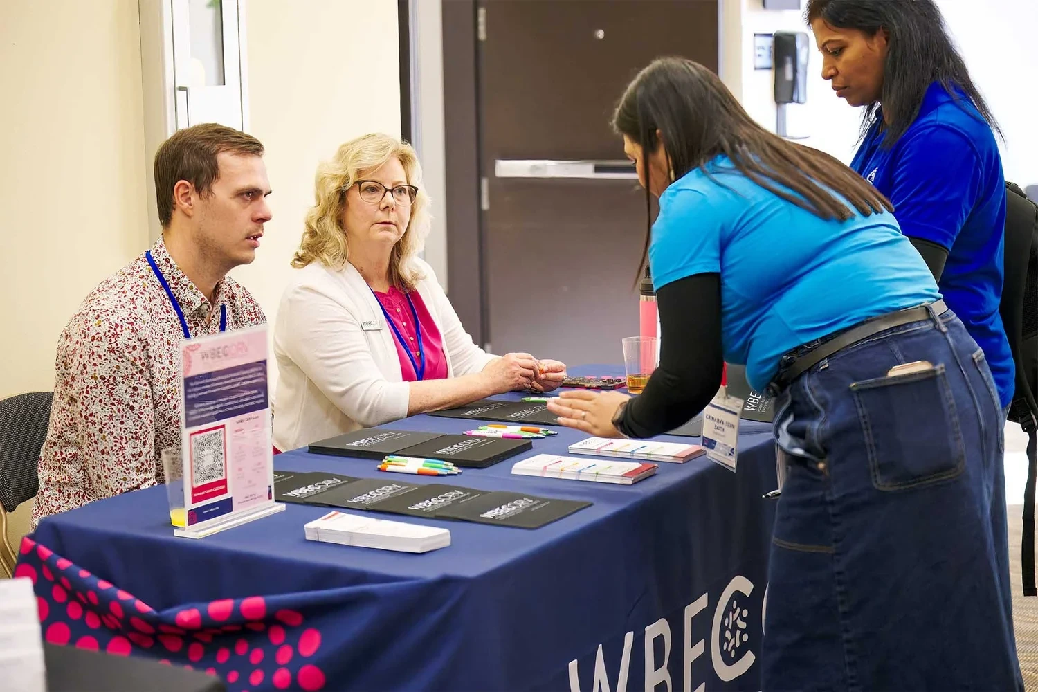 Corporate event photography by Deborah Heinlen Photography, Cincinnati — two women interacting at a branded sponsor table at a business conference