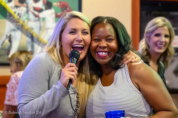 Corporate event candid photography by Deborah Heinlen Photography, Cincinnati — two women laughing and sharing a microphone at a business event