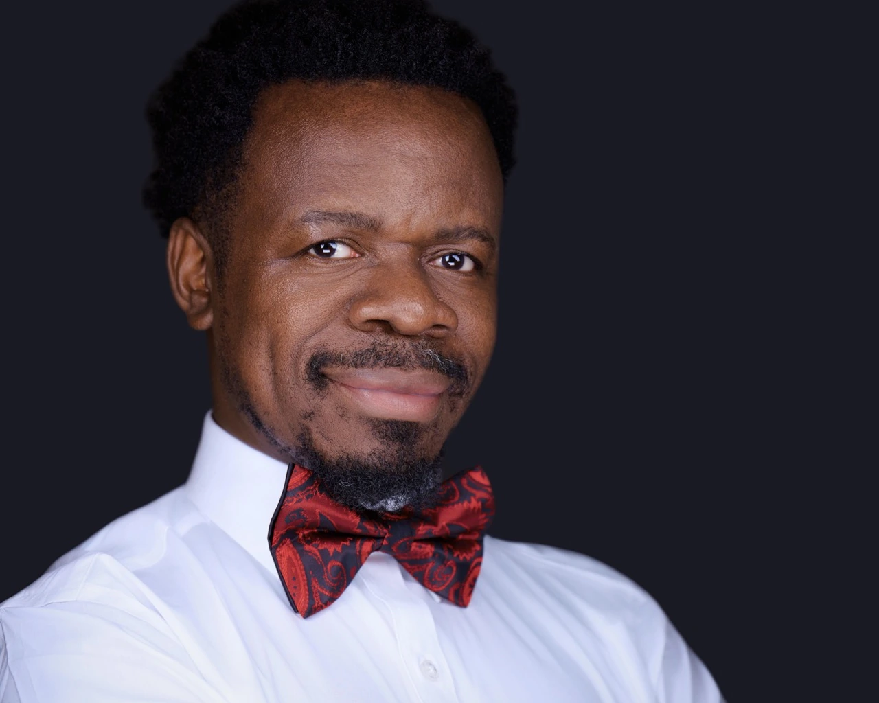 Professional male headshot by Deborah Heinlen Photography, Cincinnati — man in white dress shirt and red paisley bow tie against dark studio background