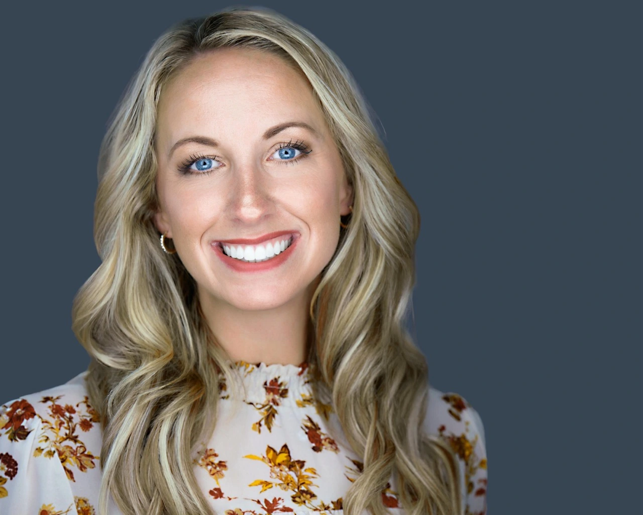 Professional female headshot by Deborah Heinlen Photography, Cincinnati — smiling woman with blonde hair in floral top against gray studio background