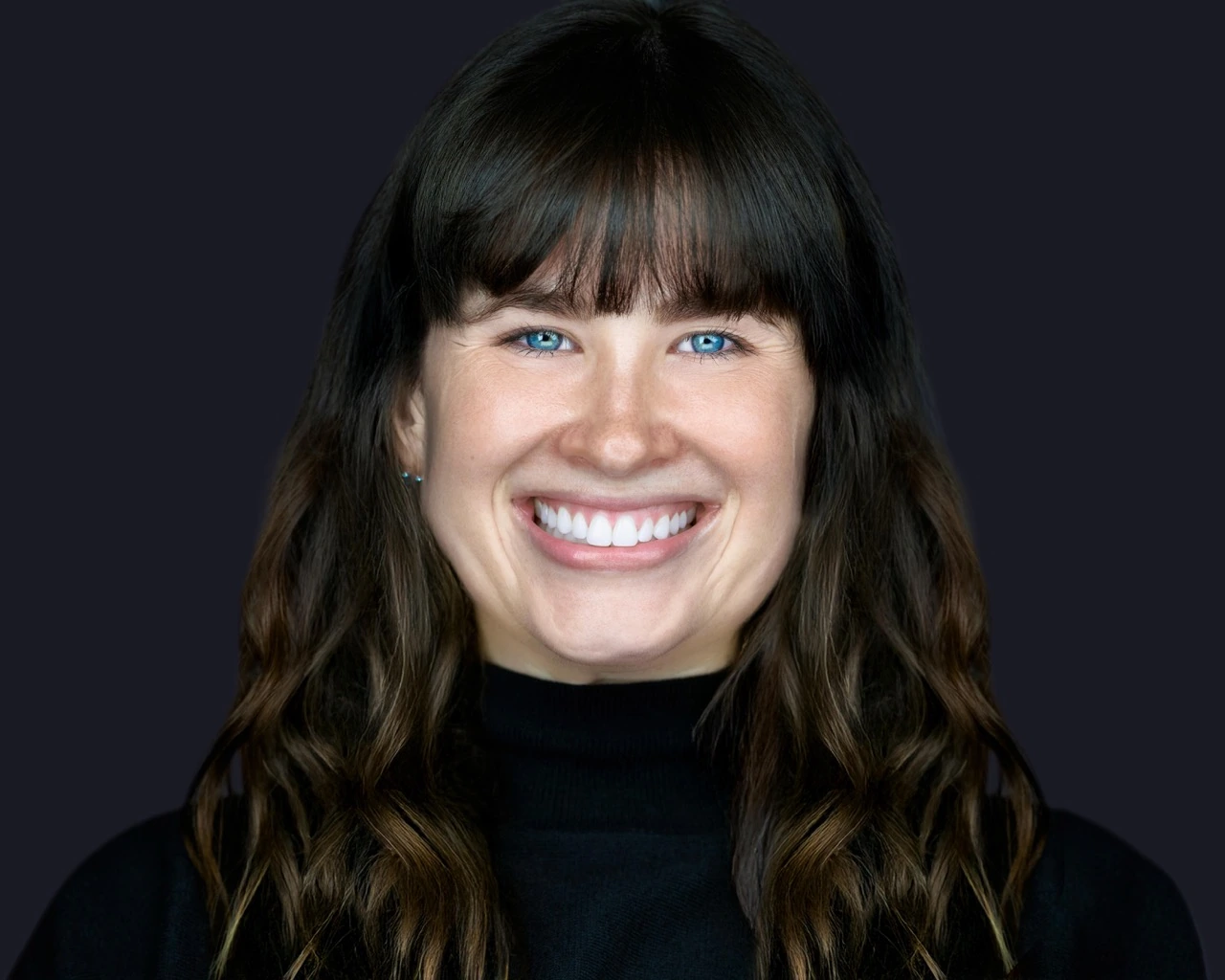 Professional female headshot by Deborah Heinlen Photography, Cincinnati — smiling woman with dark hair and bangs in black turtleneck against dark studio background