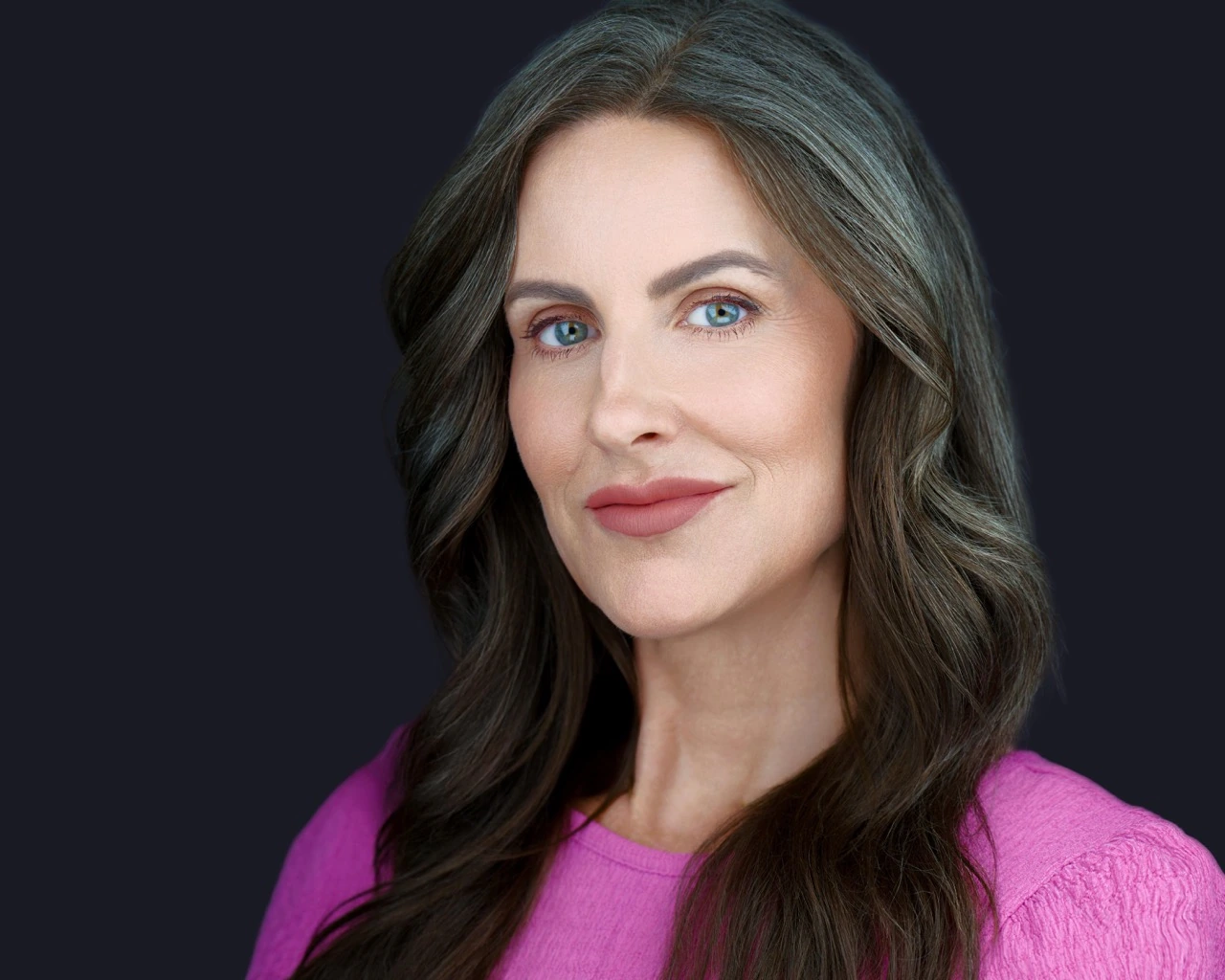 Professional female headshot by Deborah Heinlen Photography, Cincinnati — woman with long dark hair in pink top against dark studio background
