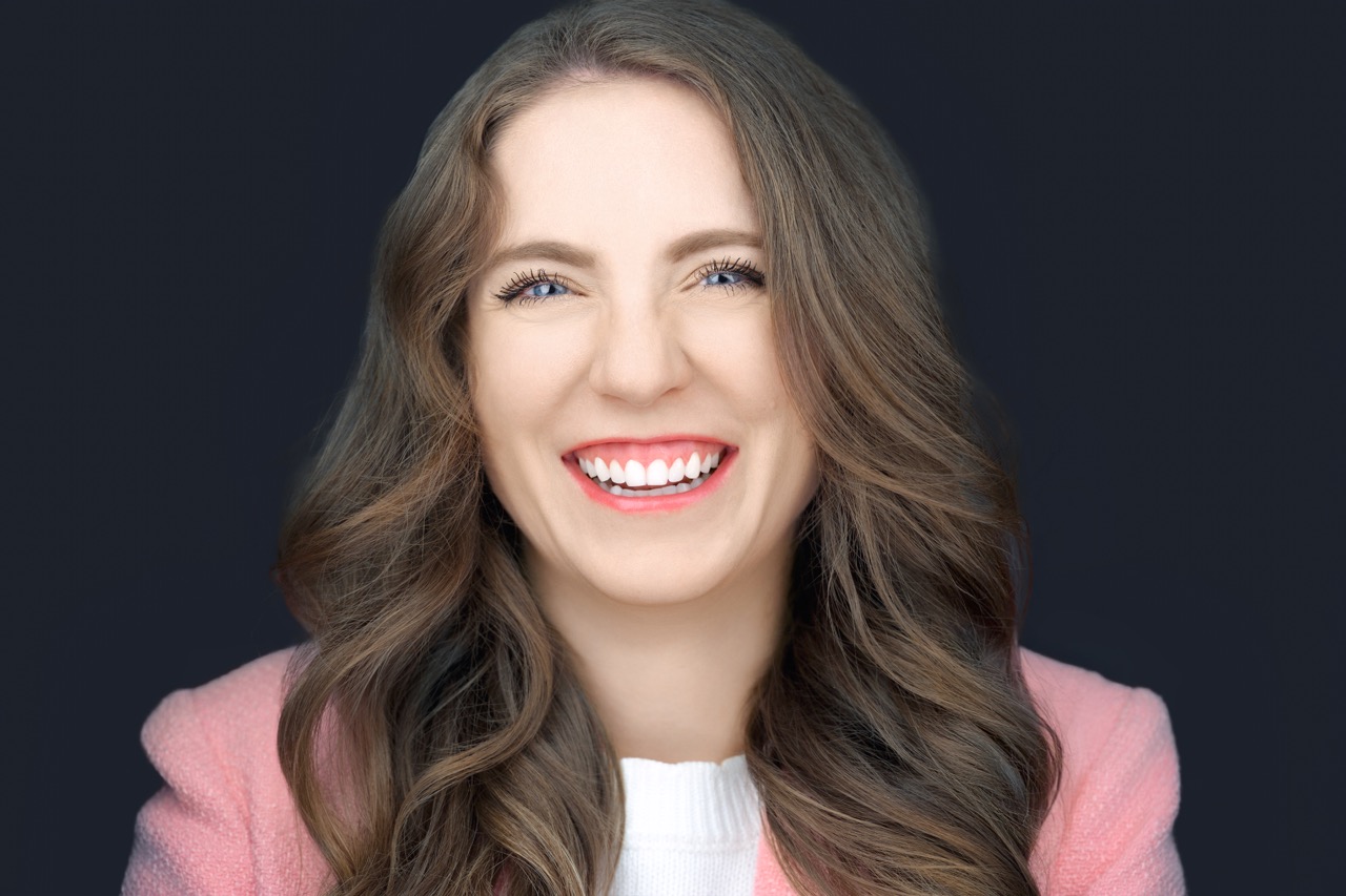 Professional headshot of a woman with dark hair and red lipstick, soft studio lighting