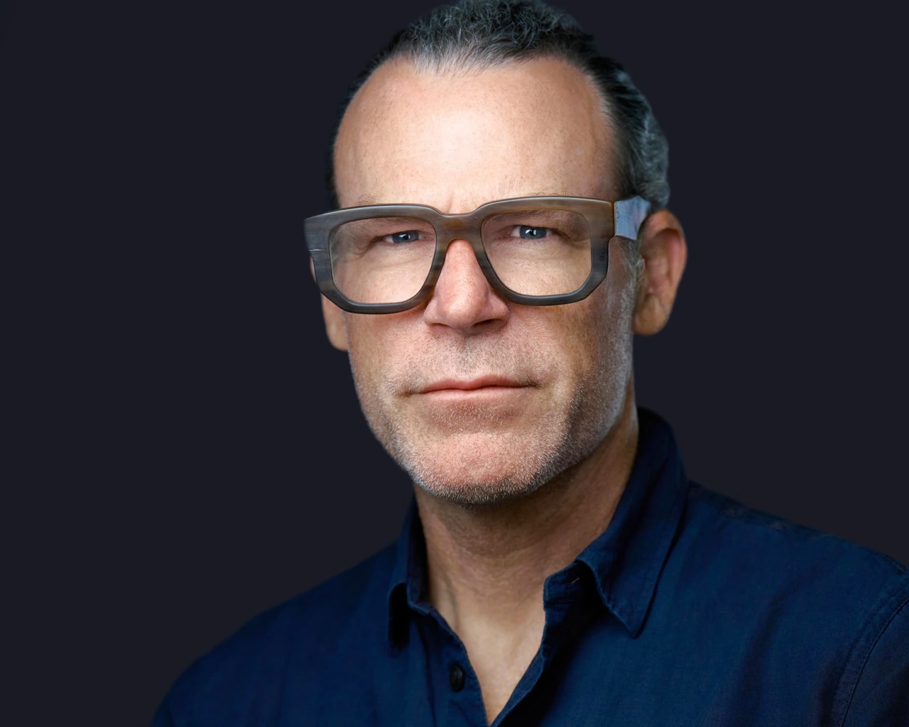 Professional male headshot by Deborah Heinlen Photography, Cincinnati — man with bold rectangular glasses and dark shirt against dark studio background