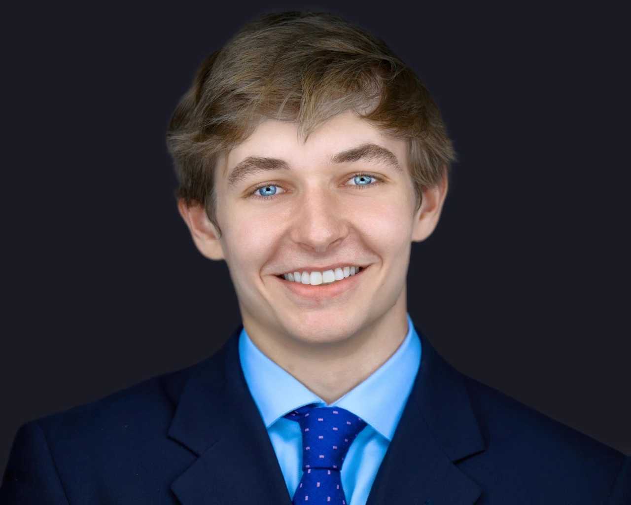Professional male headshot by Deborah Heinlen Photography, Cincinnati — smiling young man in navy suit and blue tie against dark studio background